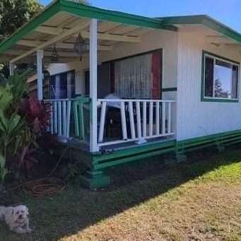 White house with green trim and porch. A small dog sits on the grass.