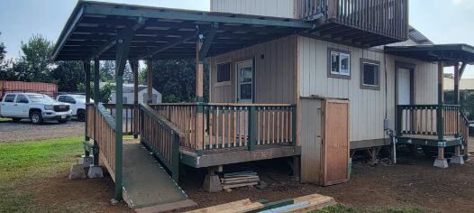 Wooden building with ramp and covered porch, two-story structure, cars in background.