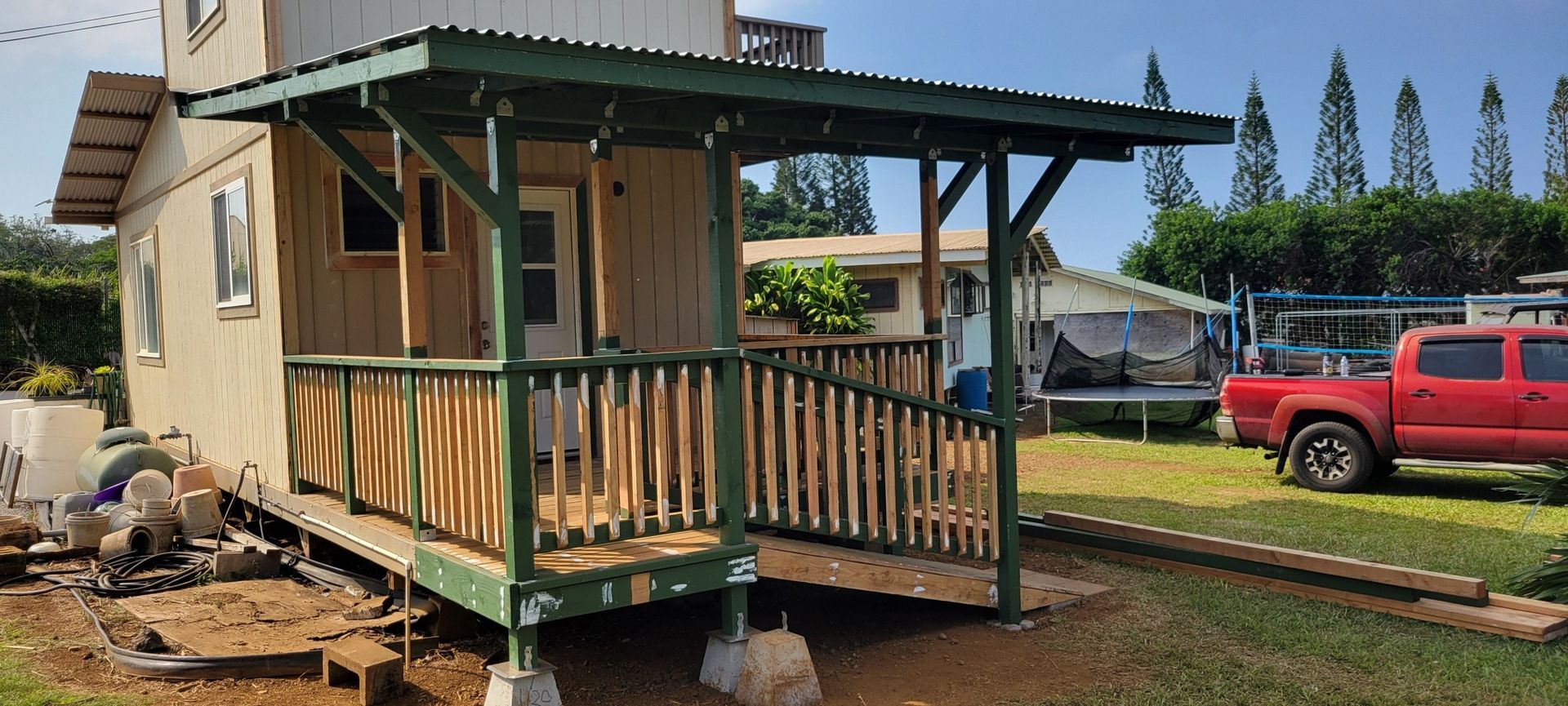 Small house with a green porch, red truck parked on the lawn, sunny day.