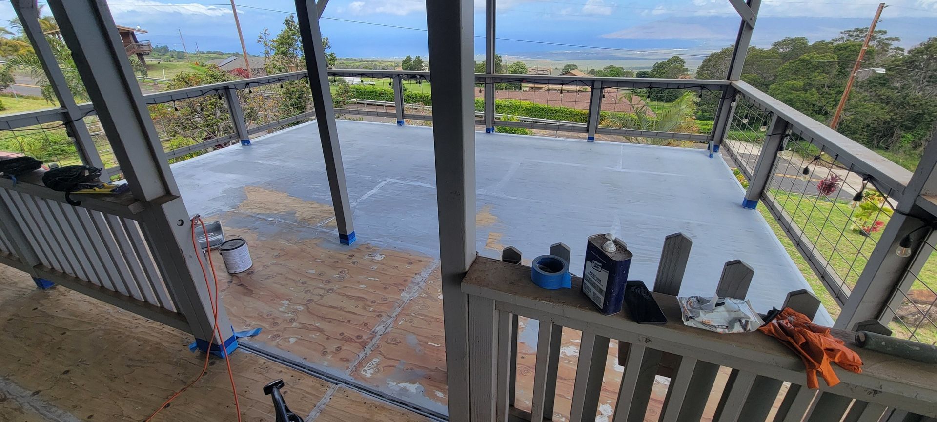 Deck being painted, overlooking ocean view. Paint can, brushes, and tools visible.