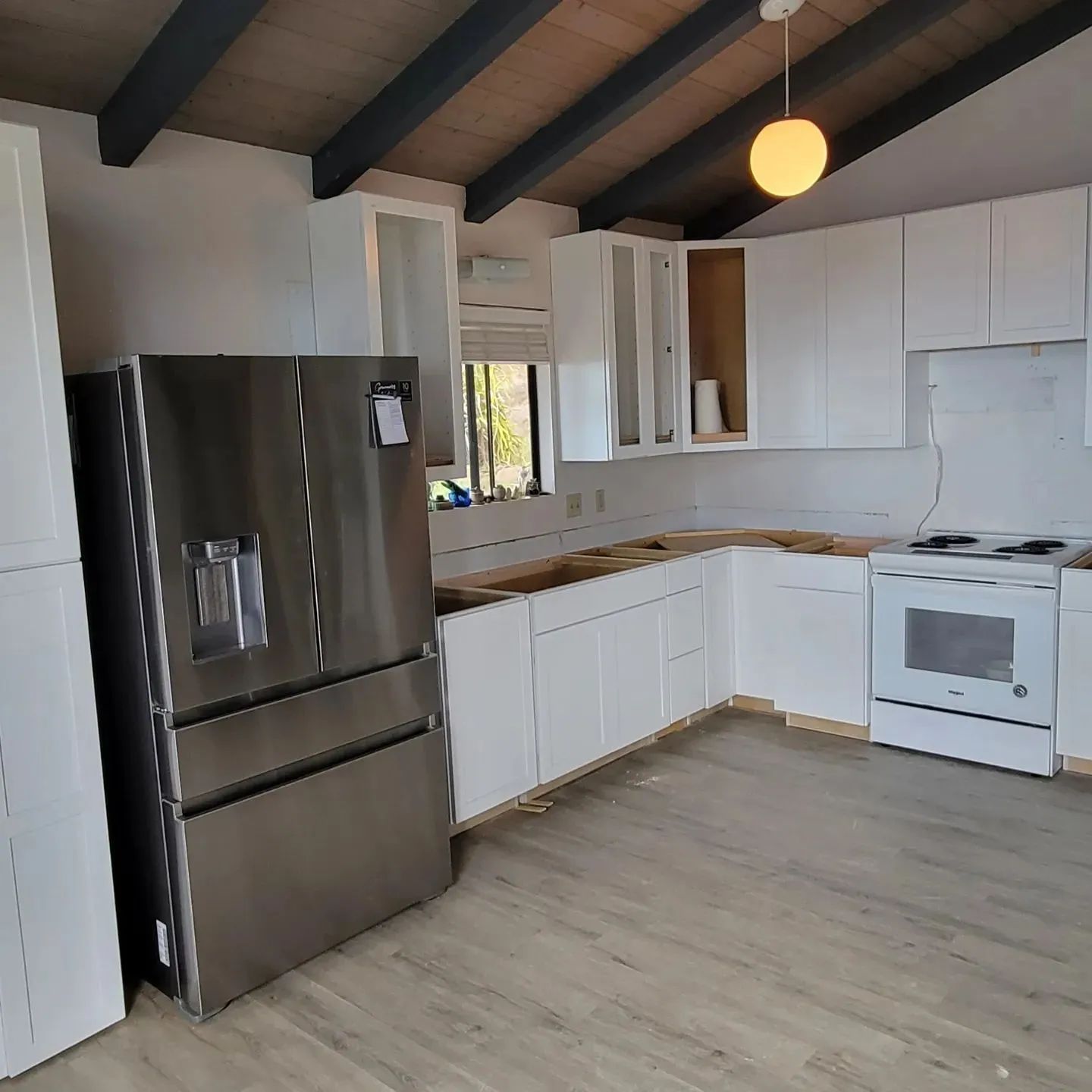 Modern white kitchen with stainless steel fridge, white cabinets, and wood ceiling beams