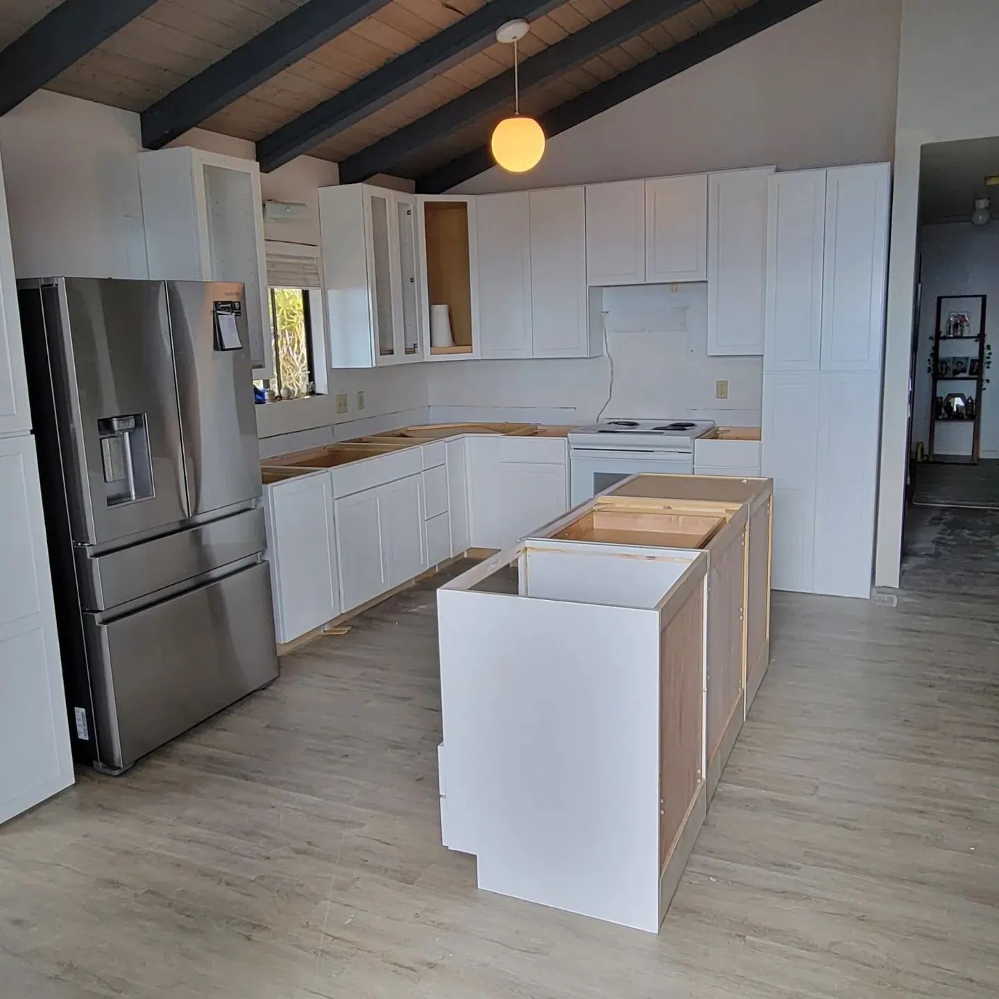 Modern kitchen with white cabinets, stainless refrigerator, and a partially finished island under a vaulted ceiling