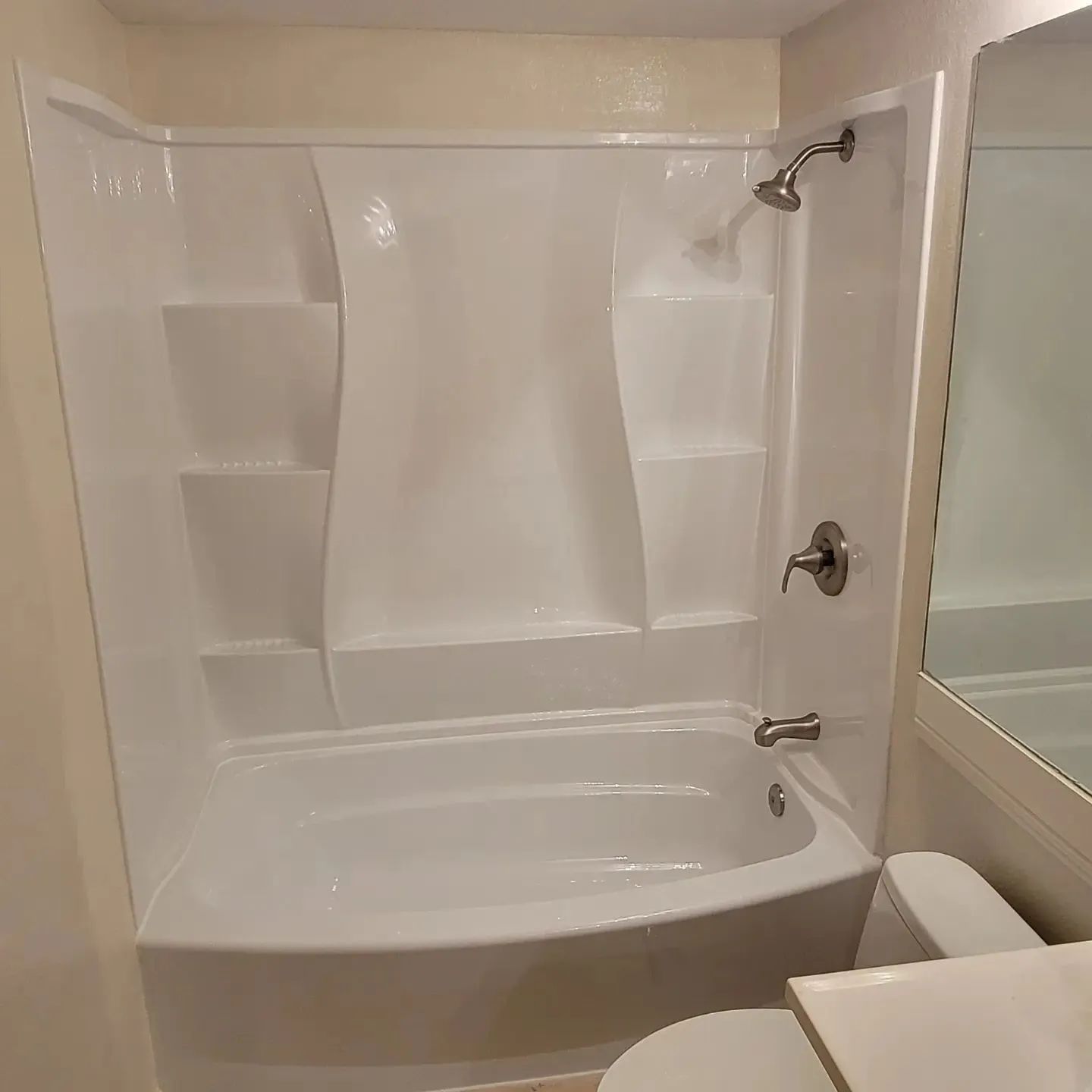 White bathtub and shower enclosure with built-in shelves and glass sliding door in a bathroom