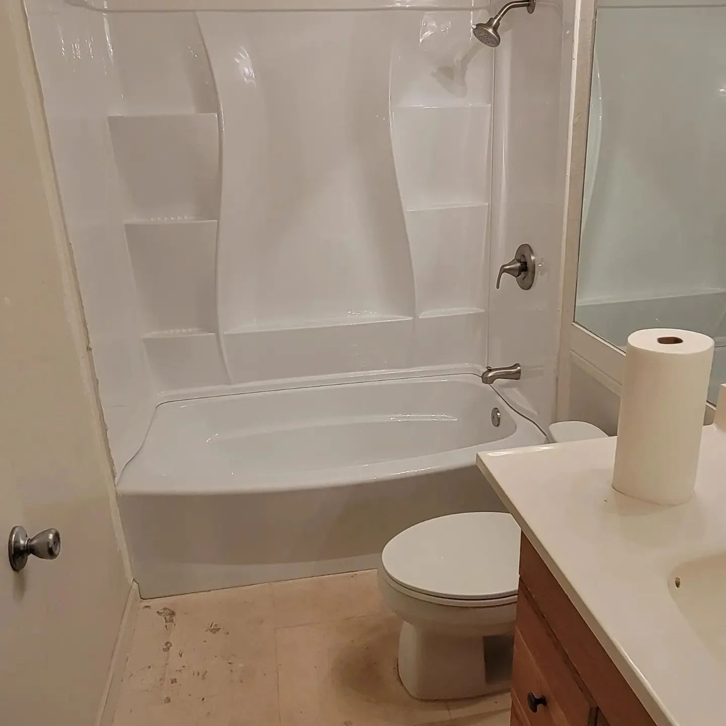 Small bathroom with tub-shower, toilet, and vanity; white walls and light wood floor.