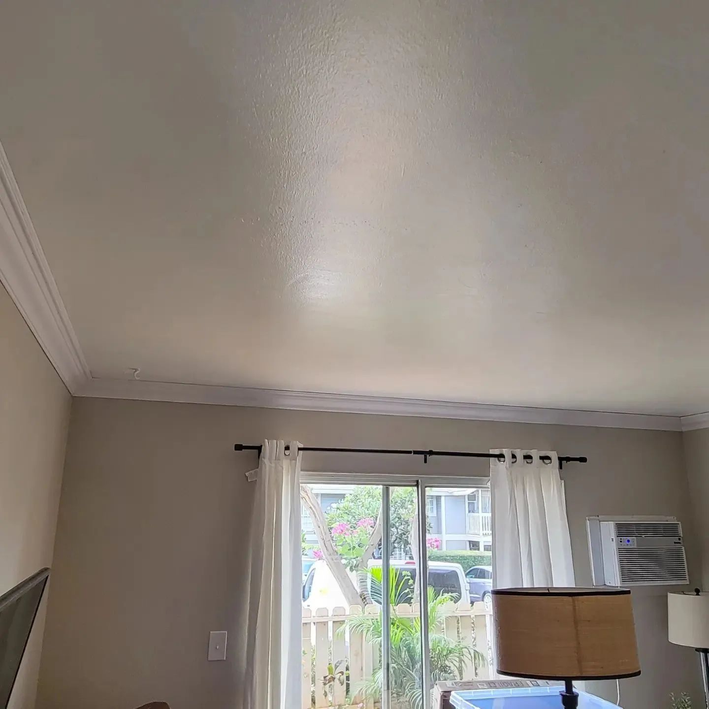 Living room ceiling with light taupe walls, white curtains, window AC unit, and a floor lamp by the window