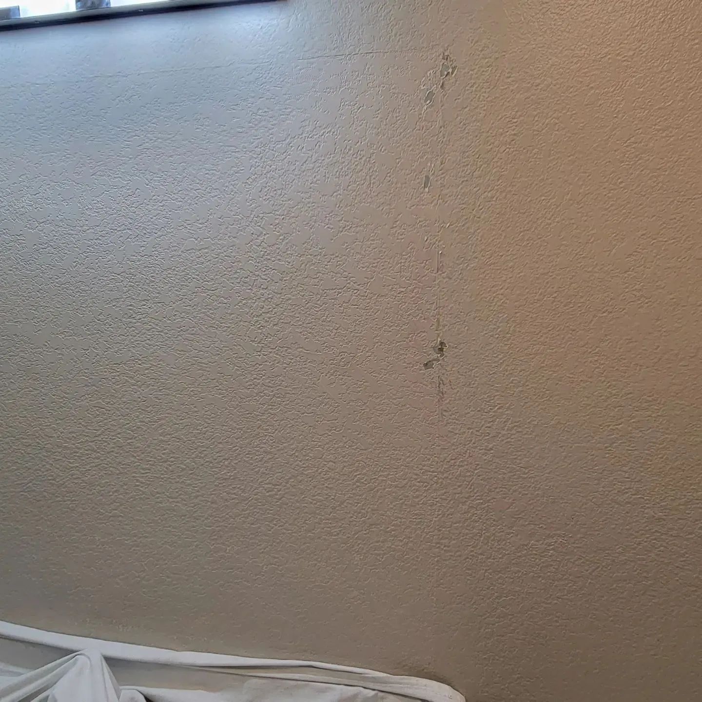 Beige textured wall with a vertical crack near the center and a bit of white fabric at the bottom left.