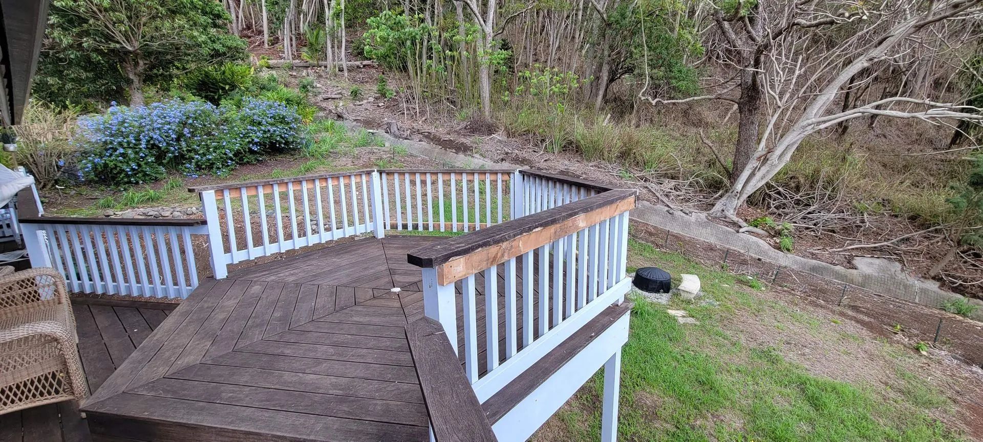 Wooden deck with white railing overlooking a grassy backyard and wooded hillside