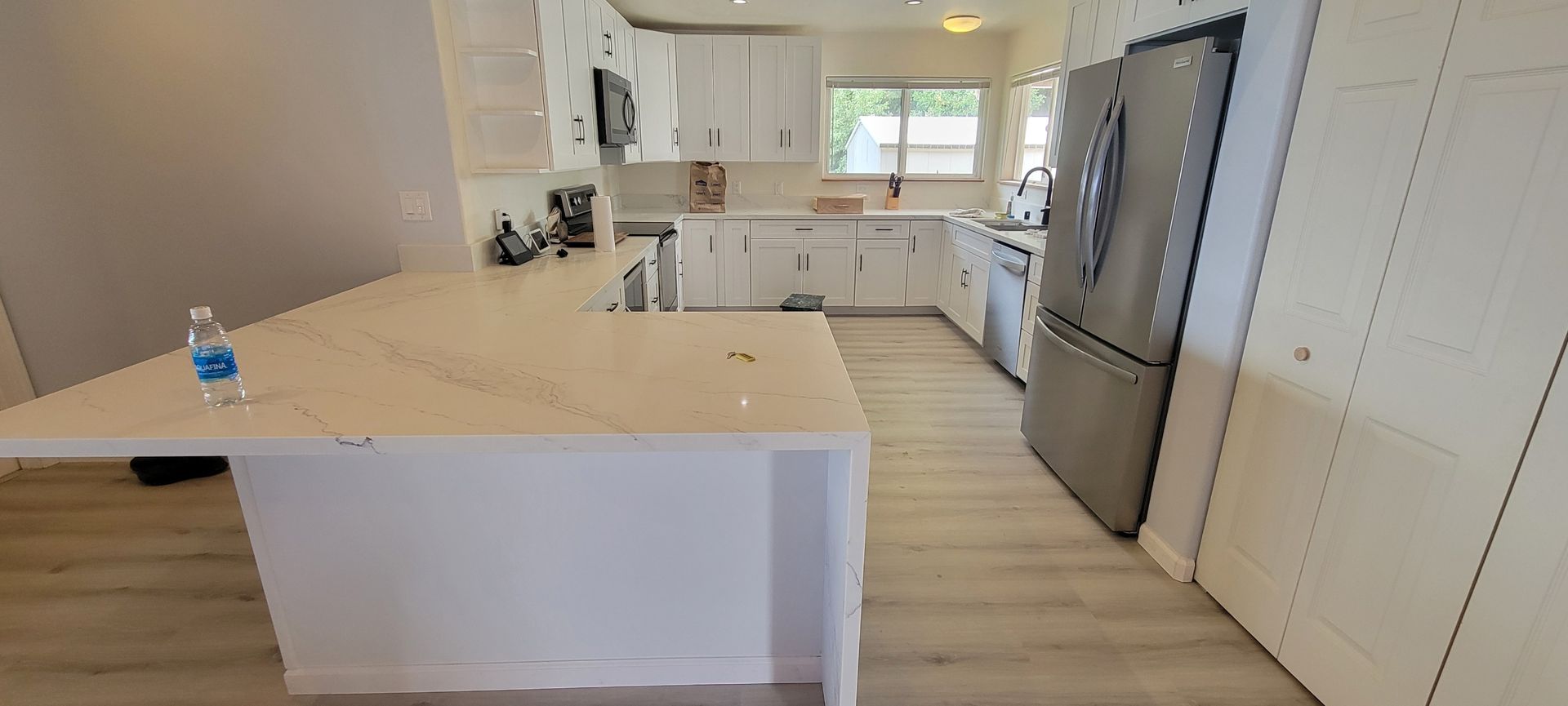 A modern white kitchen with an island, cabinets, and a stainless steel refrigerator.