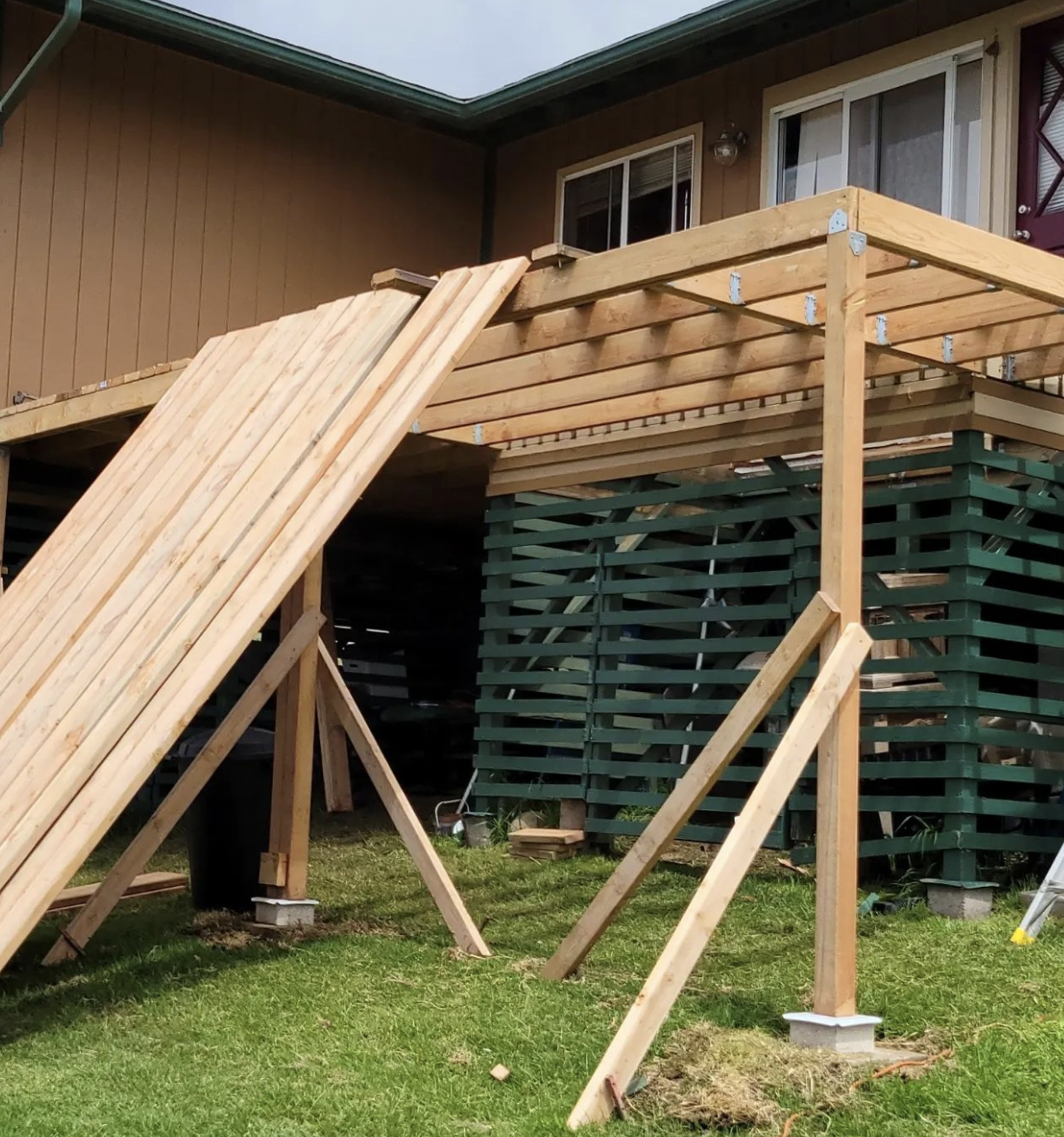Wooden pergola under construction on a grassy lawn; a person stands nearby.