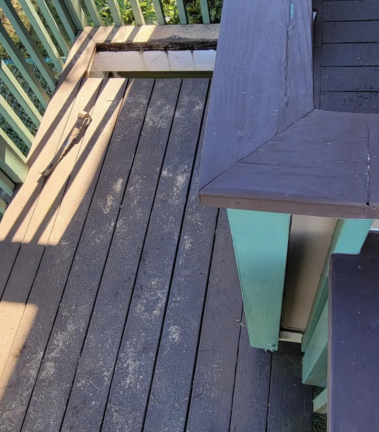 Overhead view of a deck with dark gray planks, green trim, and a lighter-colored, partially visible structure.