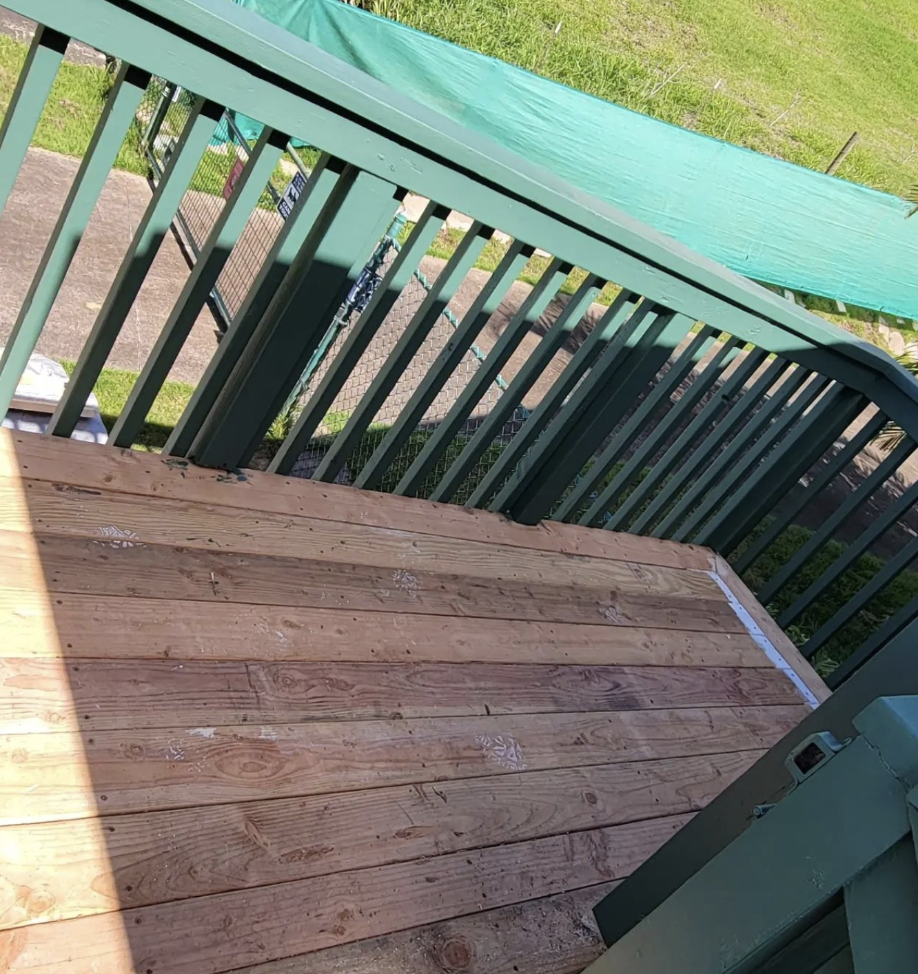 Wooden deck with green railing, leading down to grass.