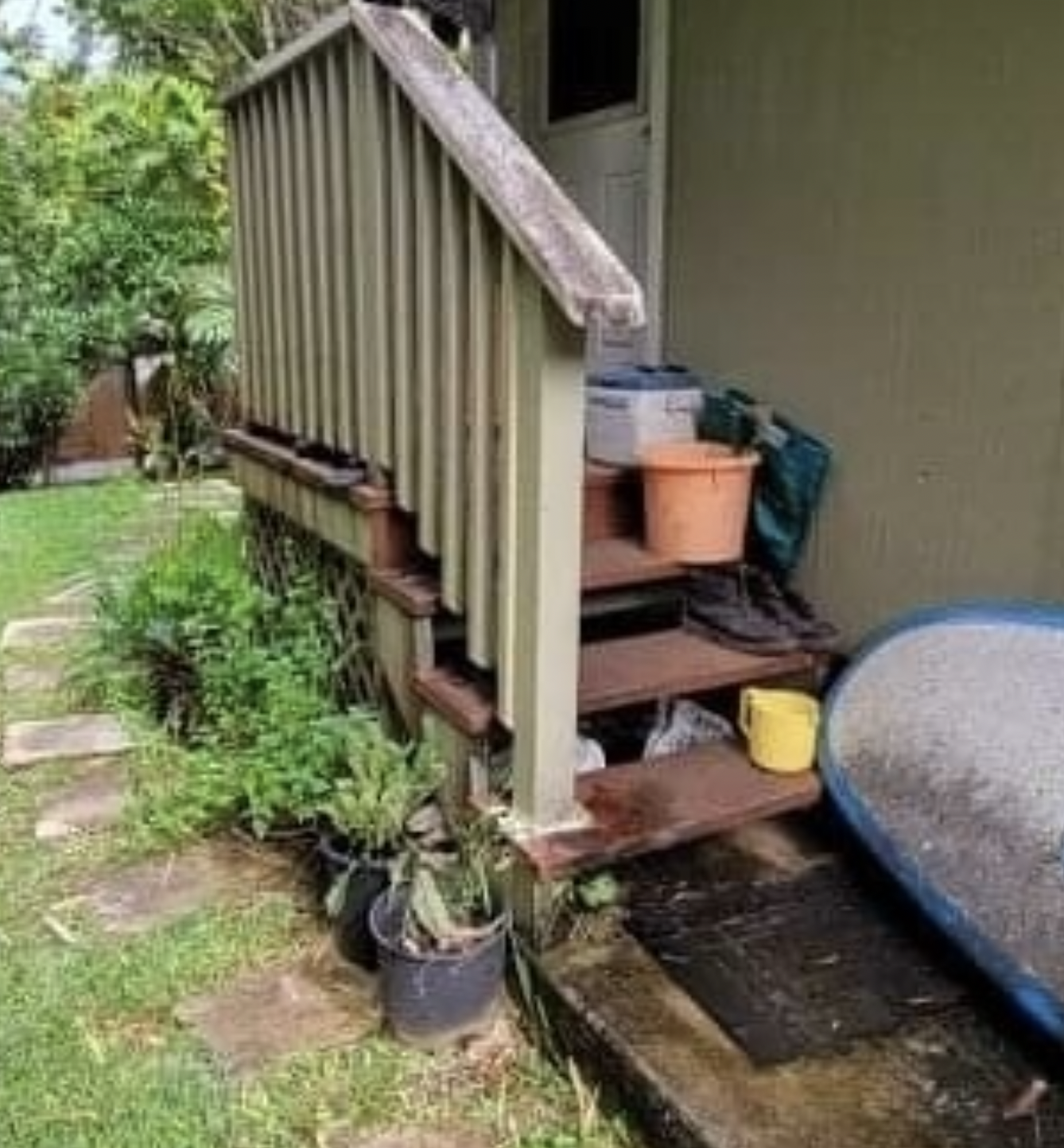 Wooden outdoor steps with a railing; potted plants line the base.