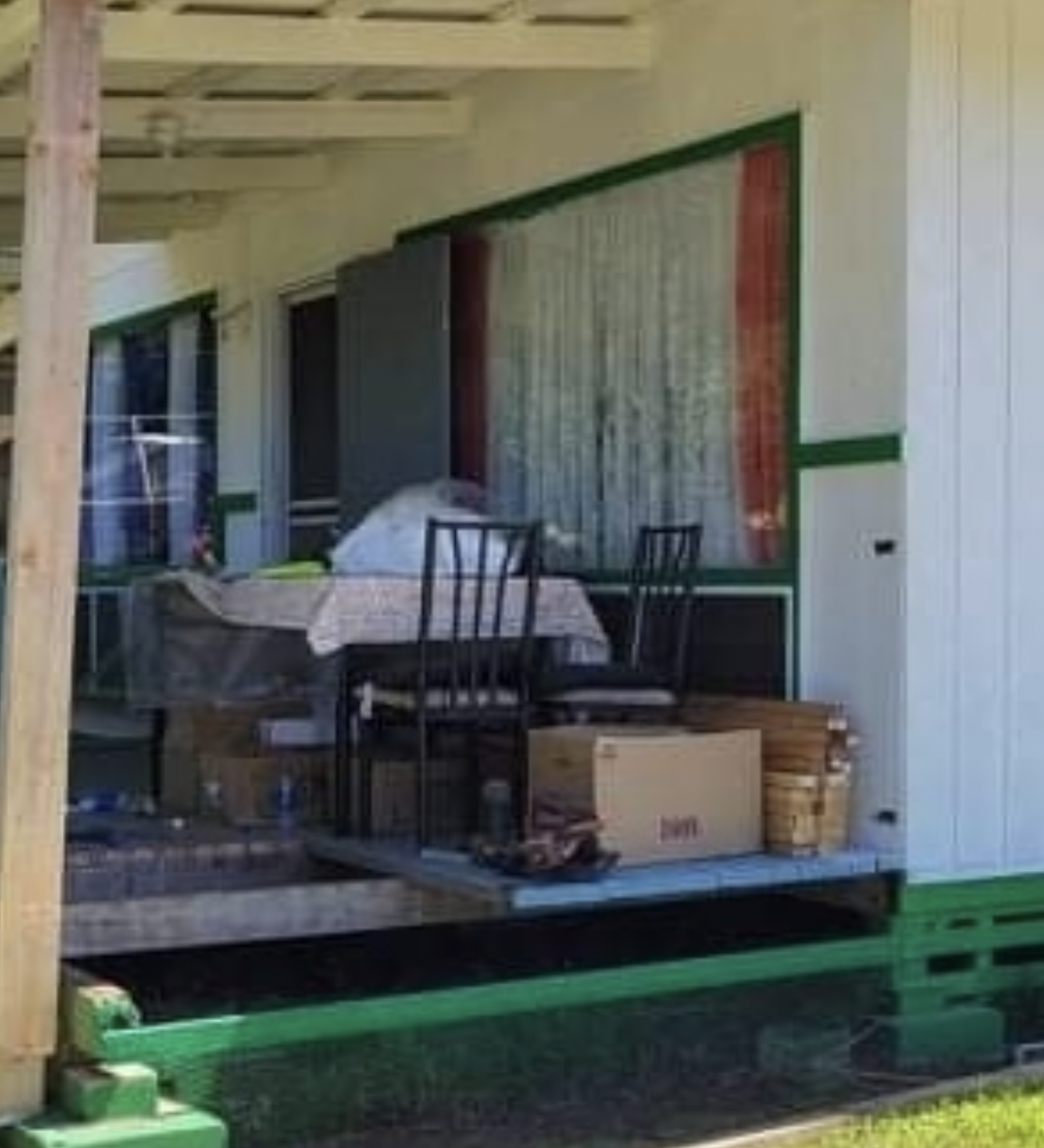 A cluttered porch with a table, chairs, and boxes. White house with green trim.