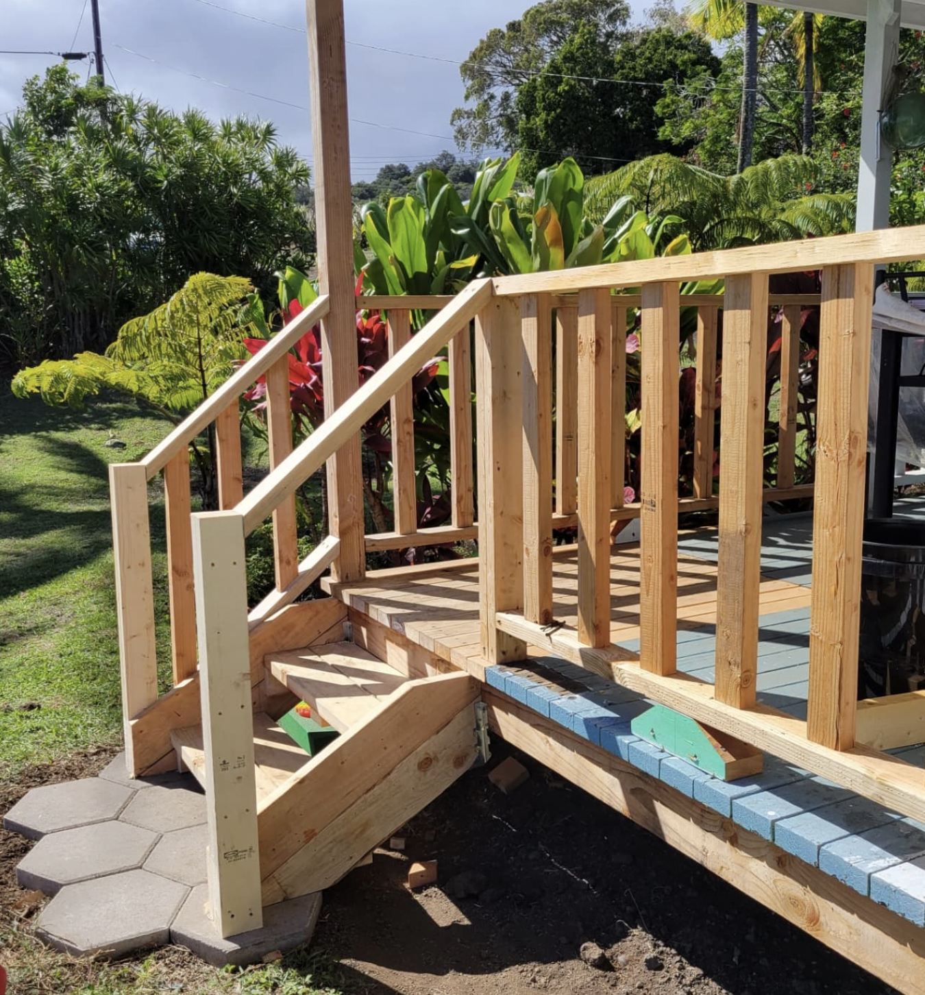 Wooden deck with steps and railing, under construction outdoors, surrounded by greenery.