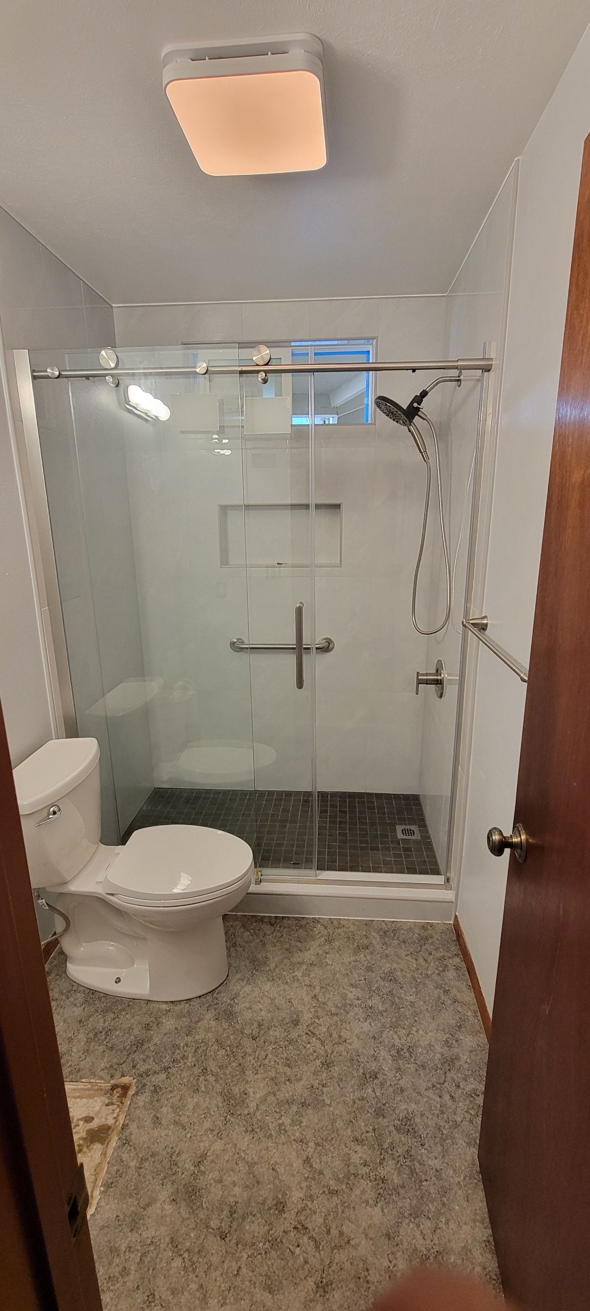 Bathroom with a white toilet, glass shower, and gray carpet.
