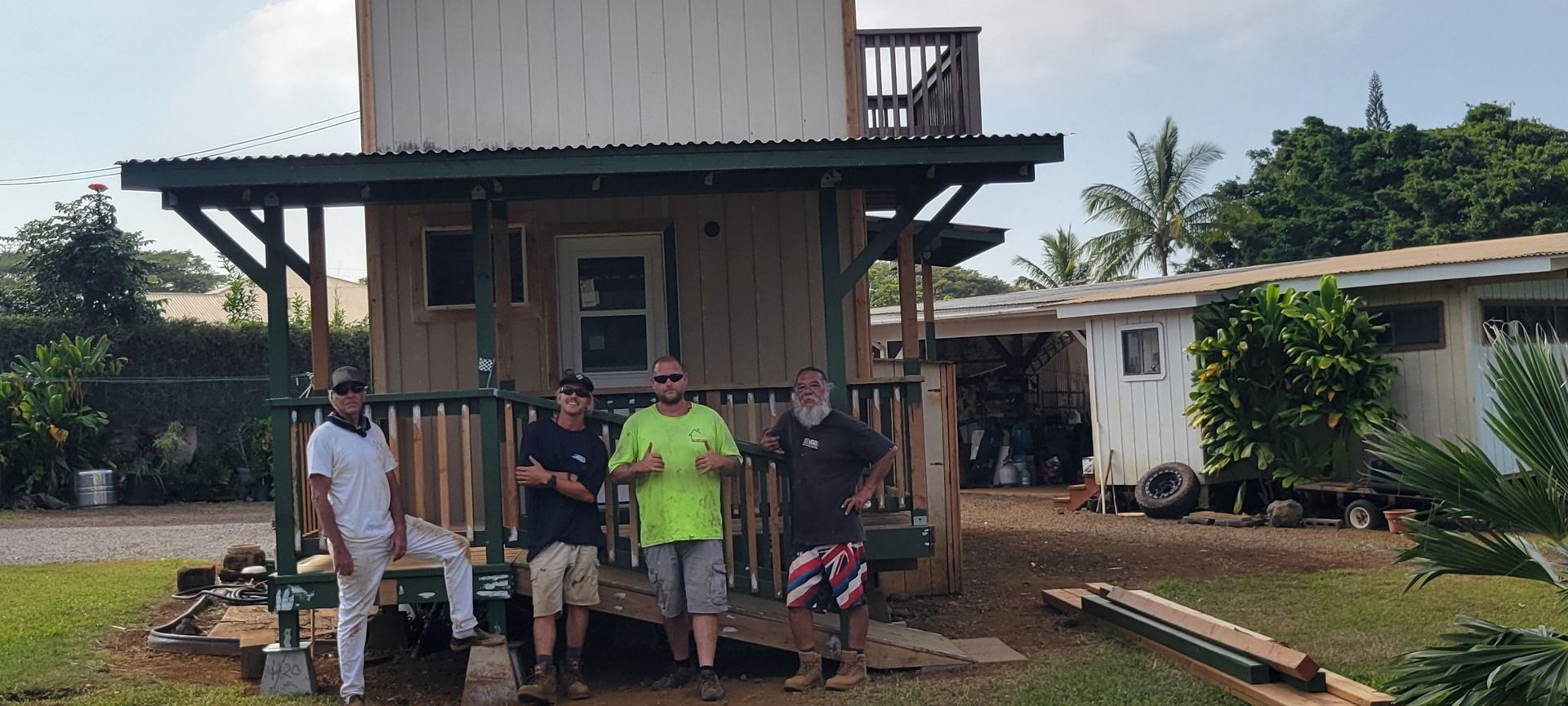 Four men stand in front of a small building with a porch.