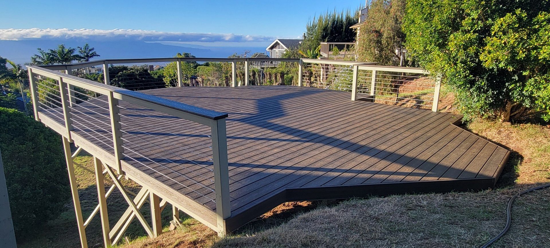 A wooden deck with a scenic view of clouds and water. It has a modern railing.