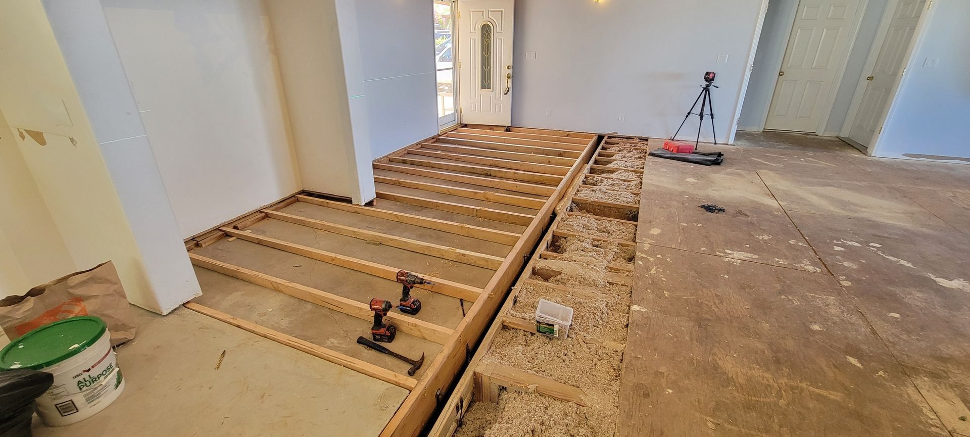 Room under renovation with exposed floor joists, wooden stairs, and construction materials.