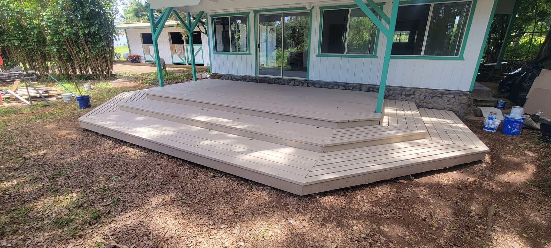 A light brown composite deck with steps in front of a white house with a green covered porch.