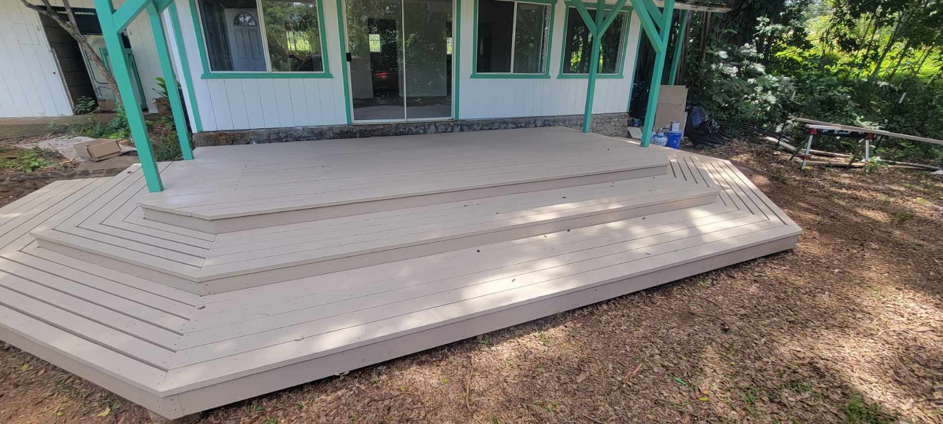 Wooden steps lead up to a house with a green awning. The steps are light brown and surrounded by dry grass.