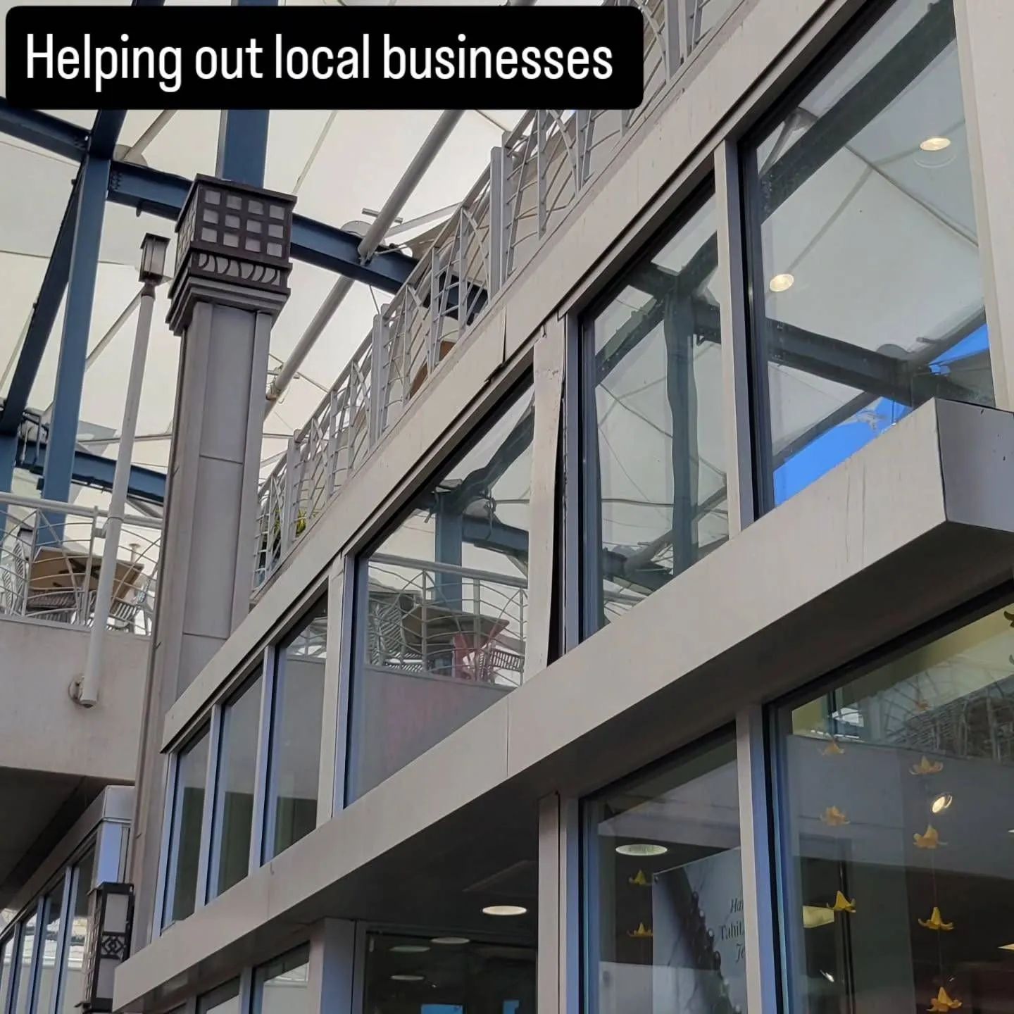 Glass-fronted building exterior with a sign reading “Helping out local businesses”