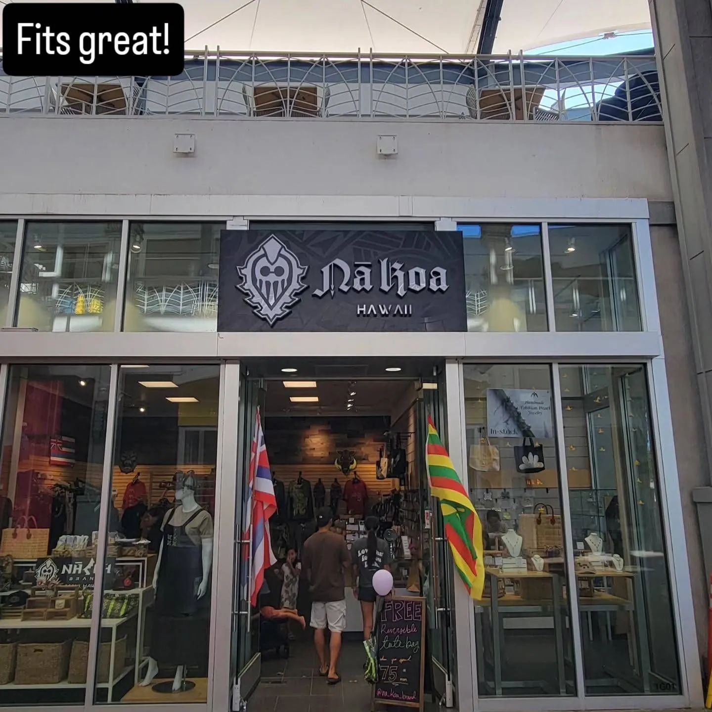 Storefront of a black-and-gray clothing shop with mannequins and flags outside, open entrance visible