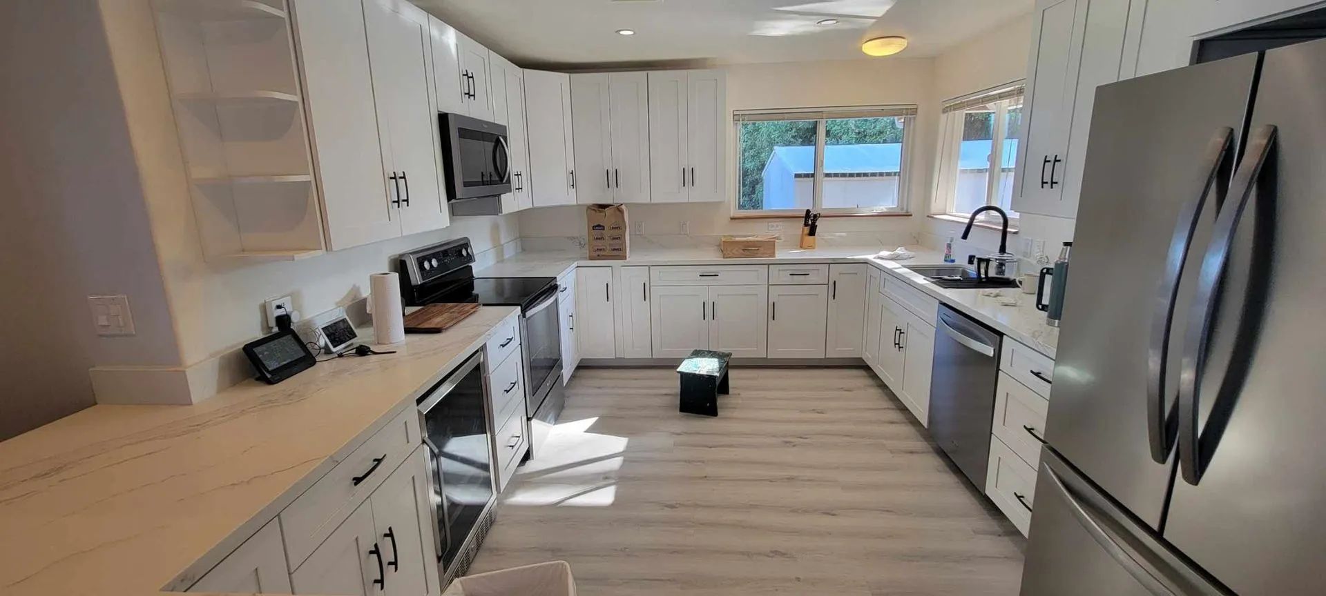 Bright modern kitchen with white cabinets, stainless steel appliances, and a small robot vacuum on the floor
