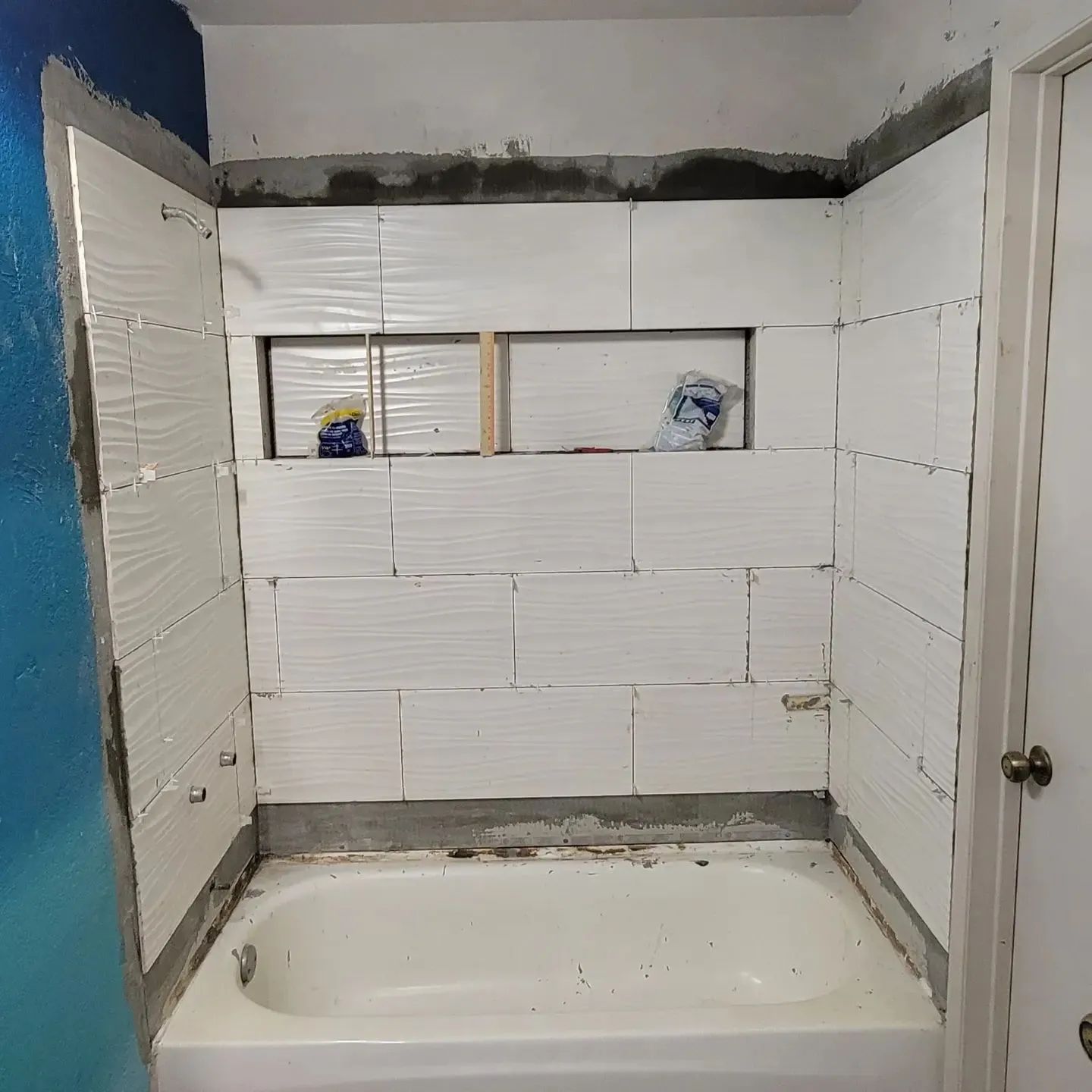 Partially tiled bathroom alcove with an open shower/tub, unfinished drywall, and two shower niches