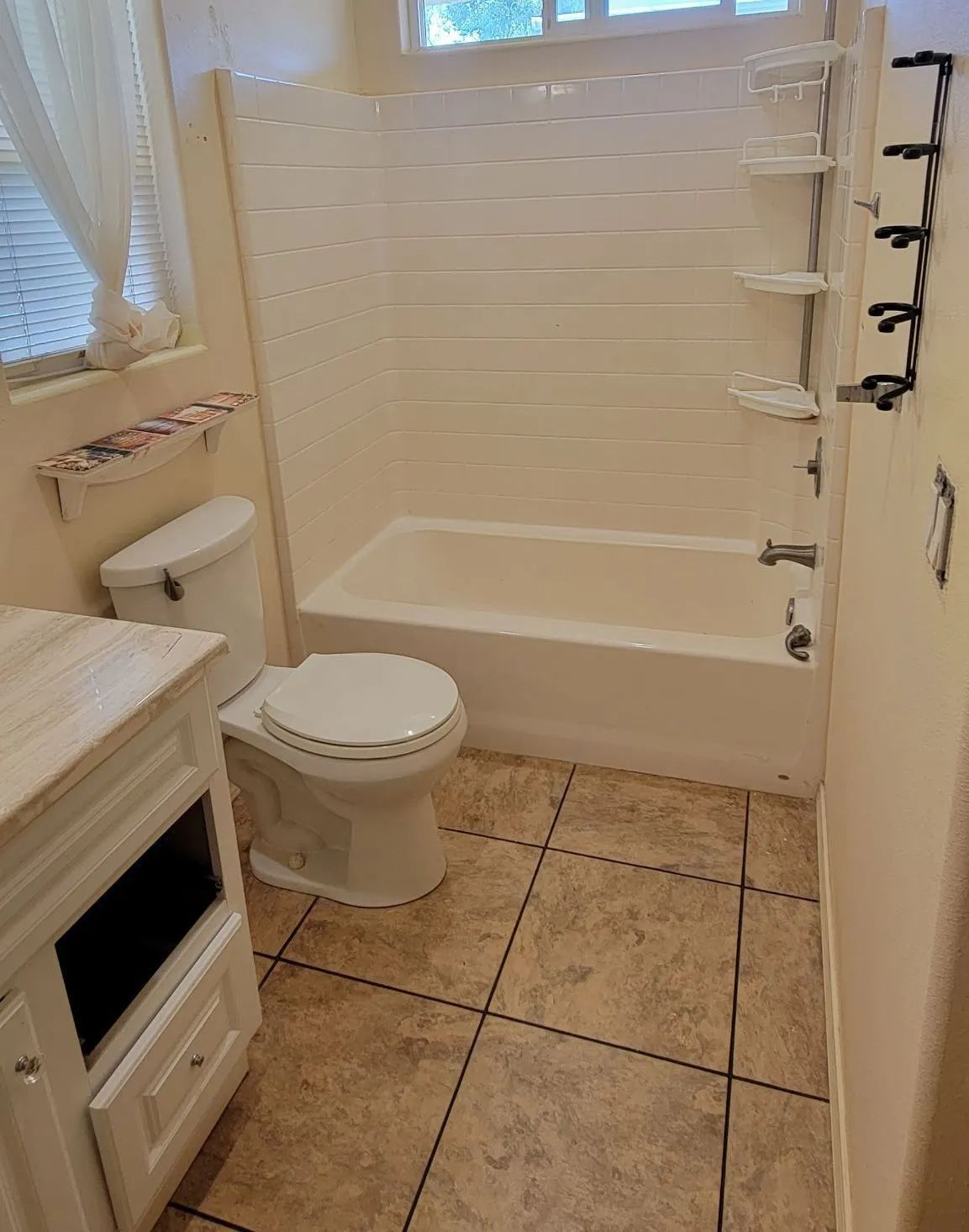 Small bathroom with toilet, bathtub, vanity, and tan tile floor, showing a shower grab bar.