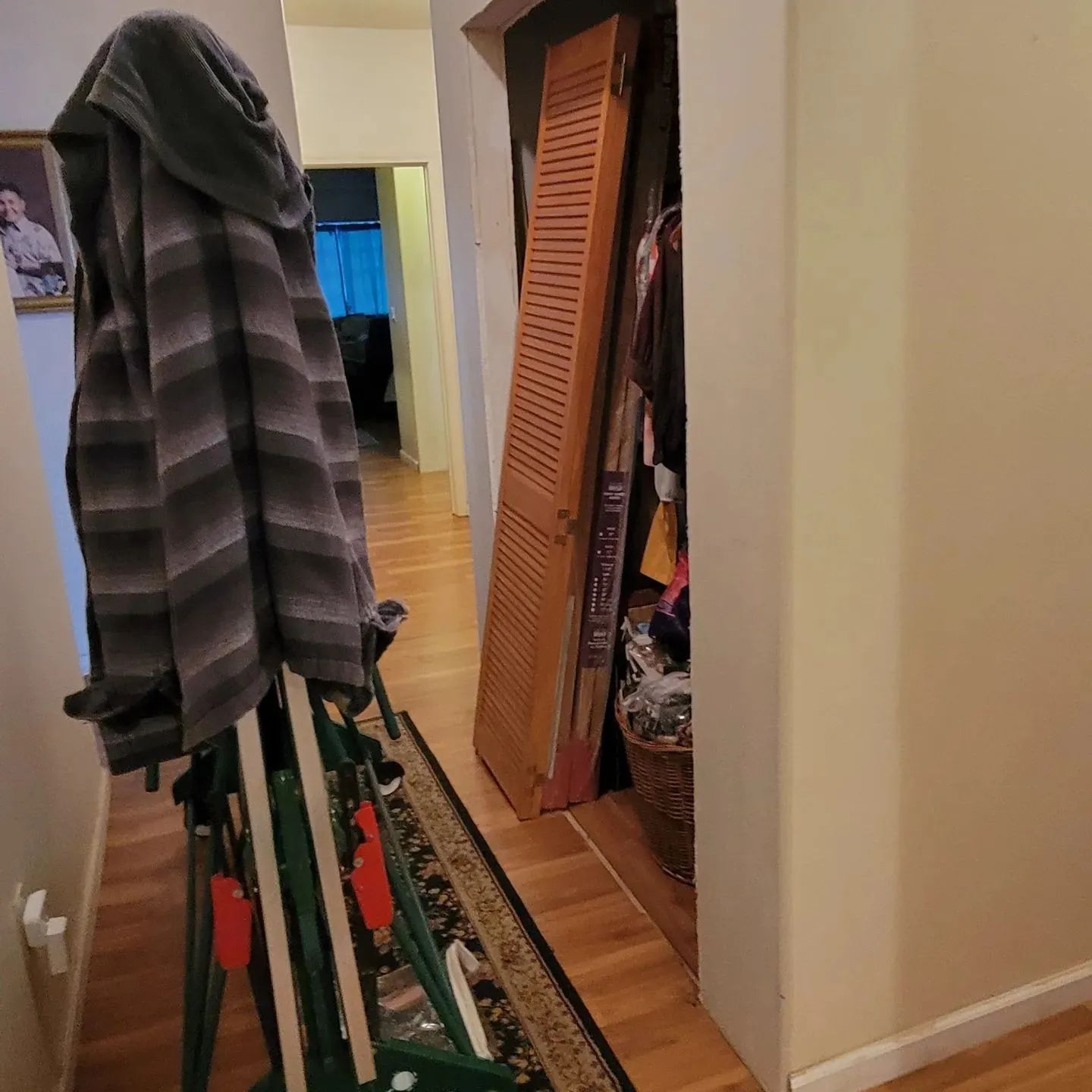 Narrow hallway with a coat rack holding a striped jacket, a rug, and an open closet door.