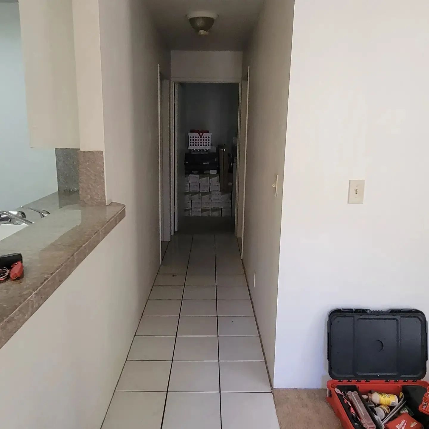 Narrow tiled hallway with a kitchen counter on the left and a black suitcase on the right near the entrance.