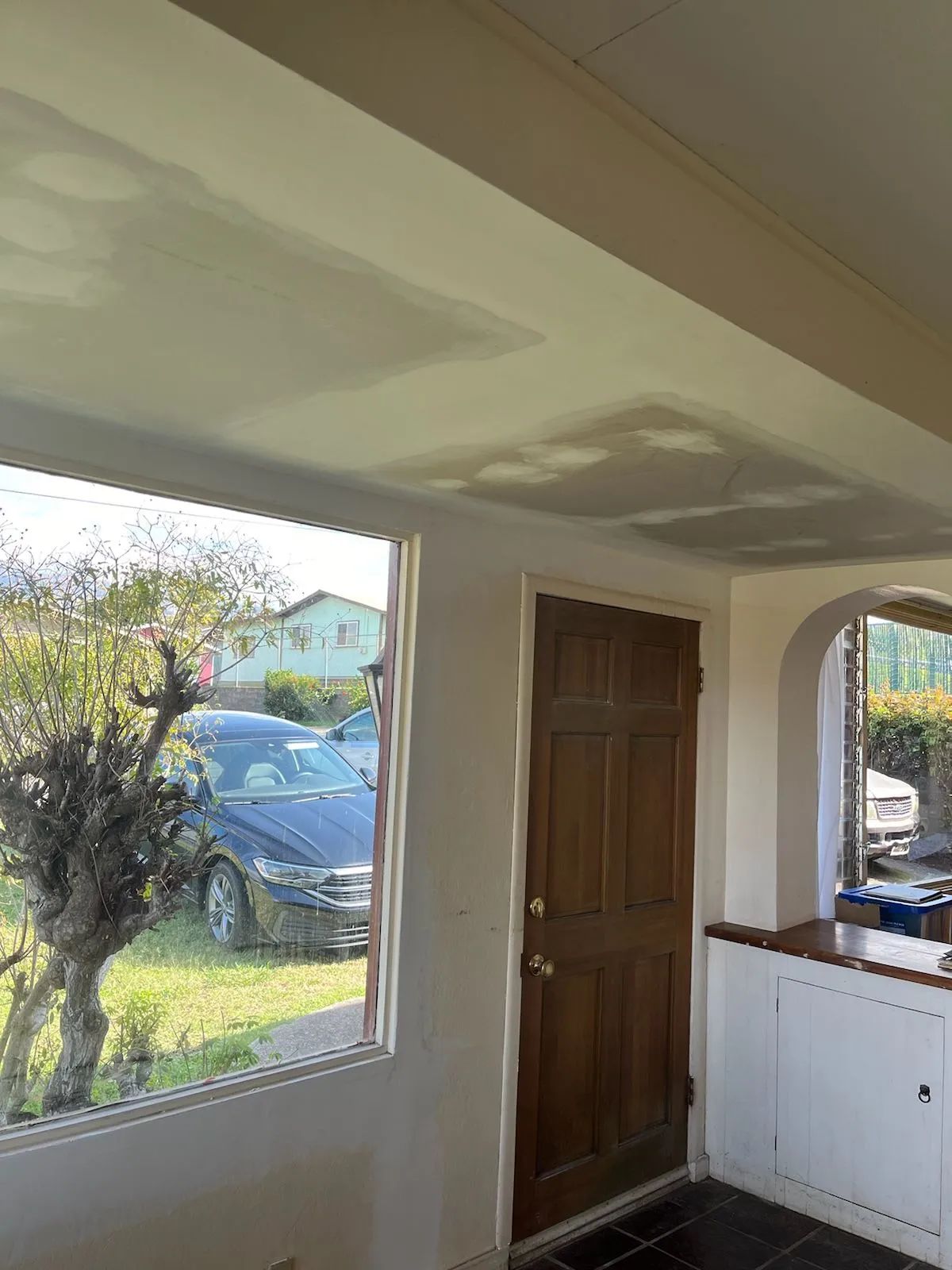 Indoor porch with a wooden front door, window, and cabinet, looking out to a parked car and tree outside