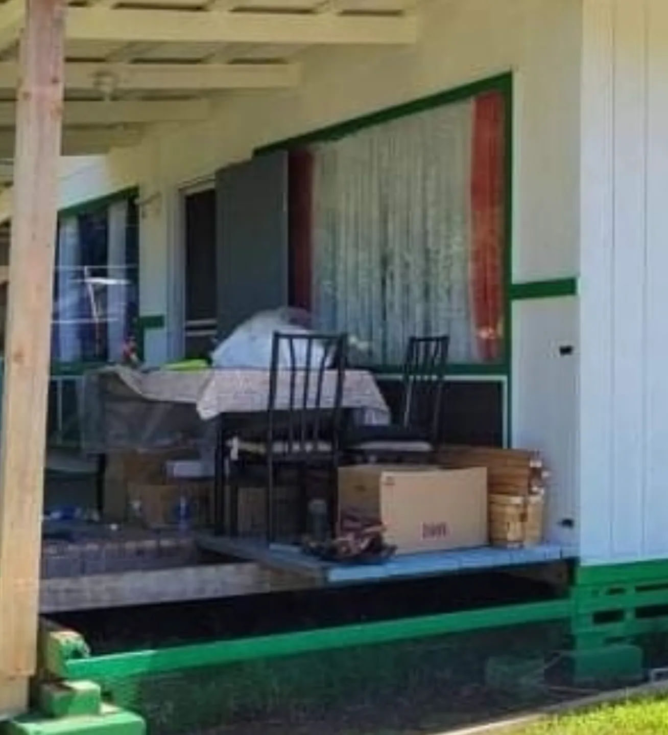 Porch with table, chairs, and boxes under a white roof with green trim