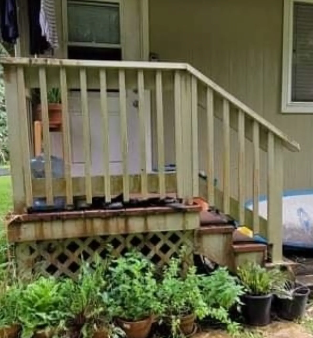 Front porch with wooden railing, stairs, potted plants, and lattice skirting on a house.