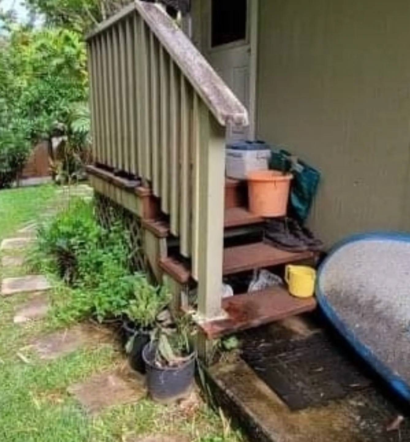 Outdoor porch stairs beside a house, with potted plants and buckets on the steps