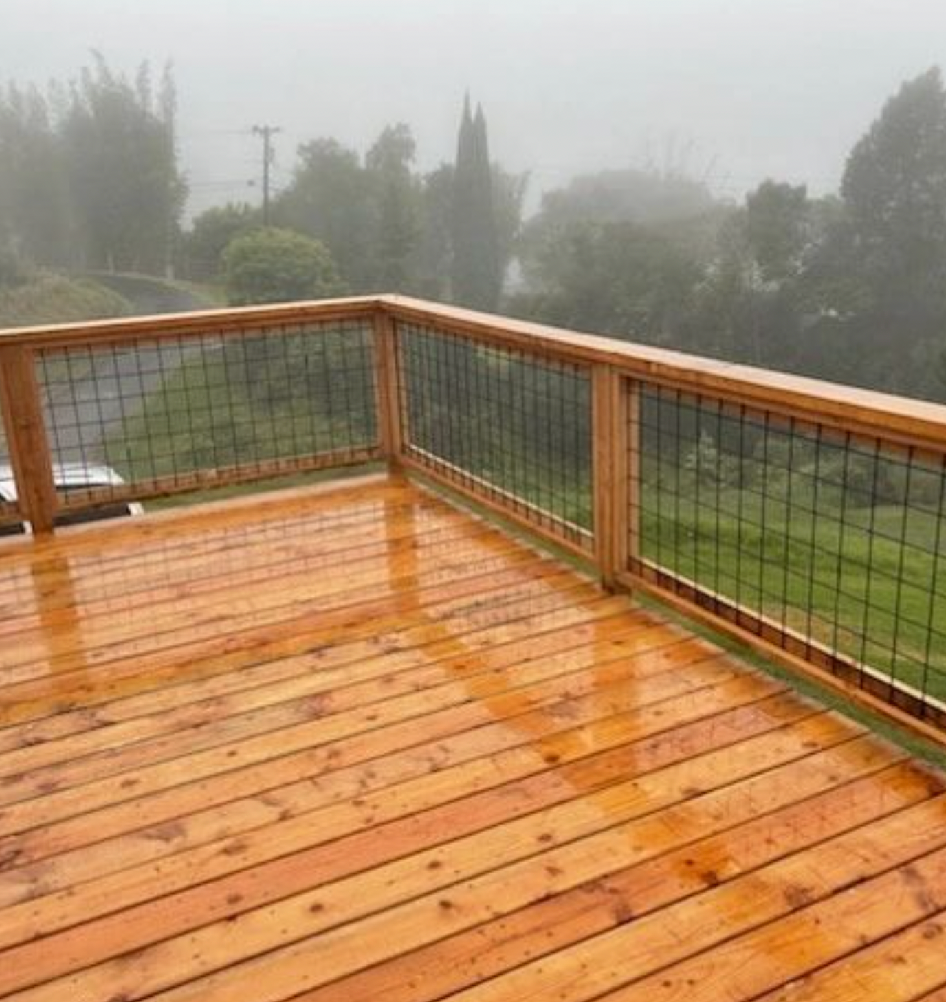 Rain-soaked wooden deck with wire railing overlooking a foggy green landscape