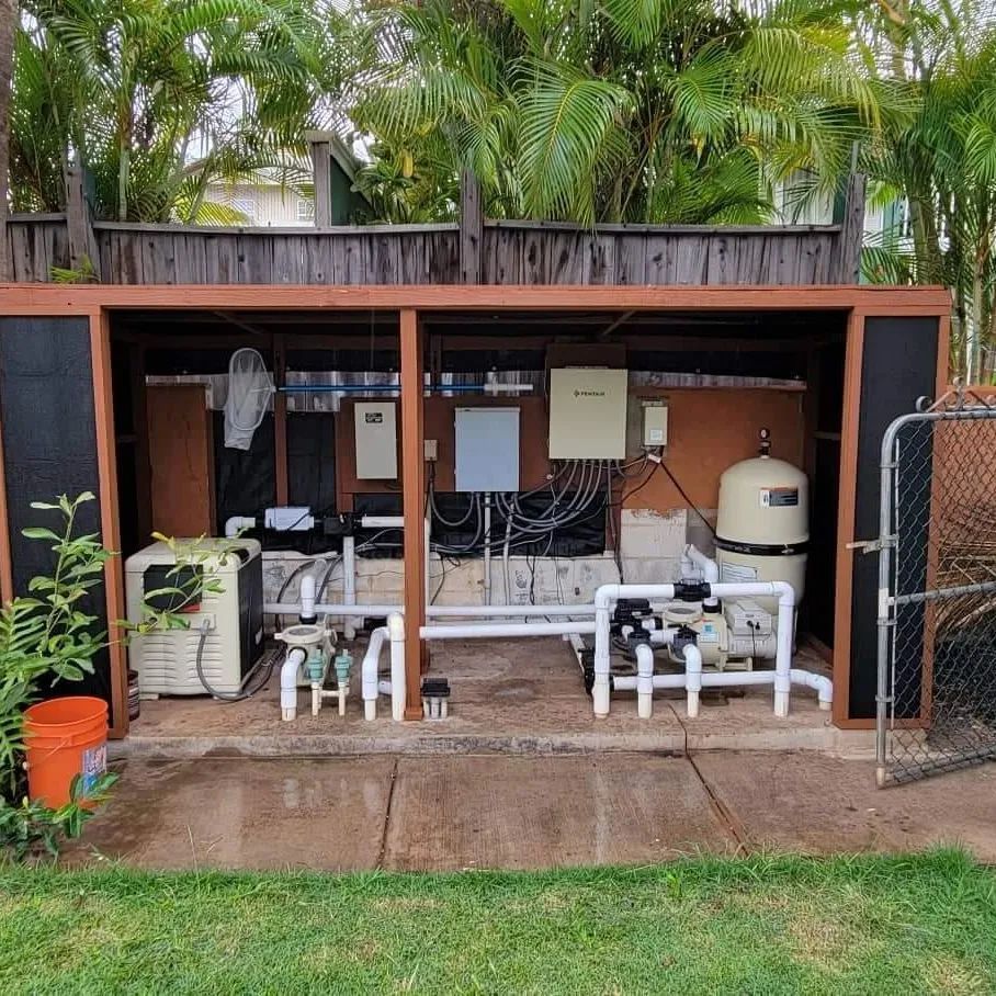 Outdoor pool equipment area with pumps, pipes, and a filtration tank under a wooden shed.