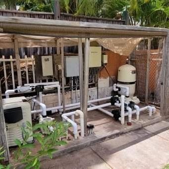 Outdoor pool equipment with white pipes, tanks, and pumps under a wooden shelter