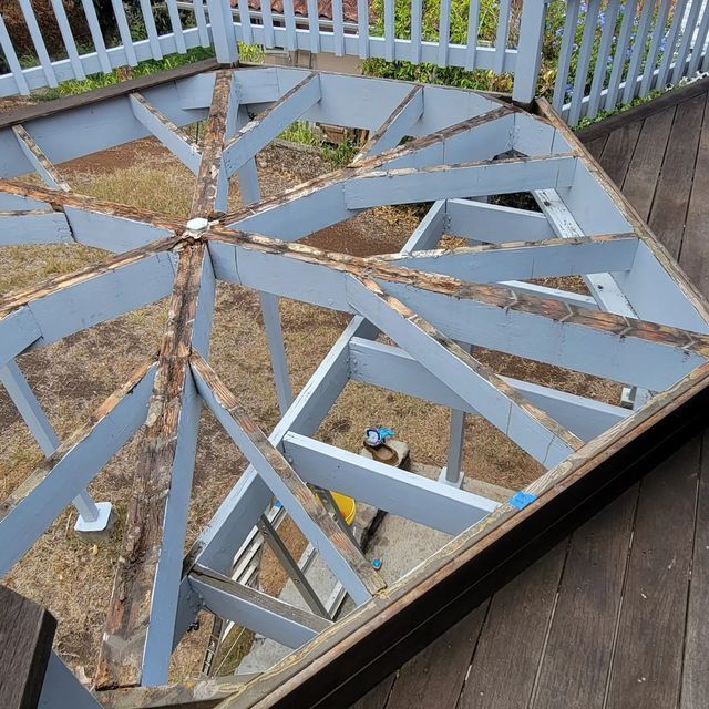 Broken glass-top patio table with cracked blue slats on a wooden deck, showing the ground below