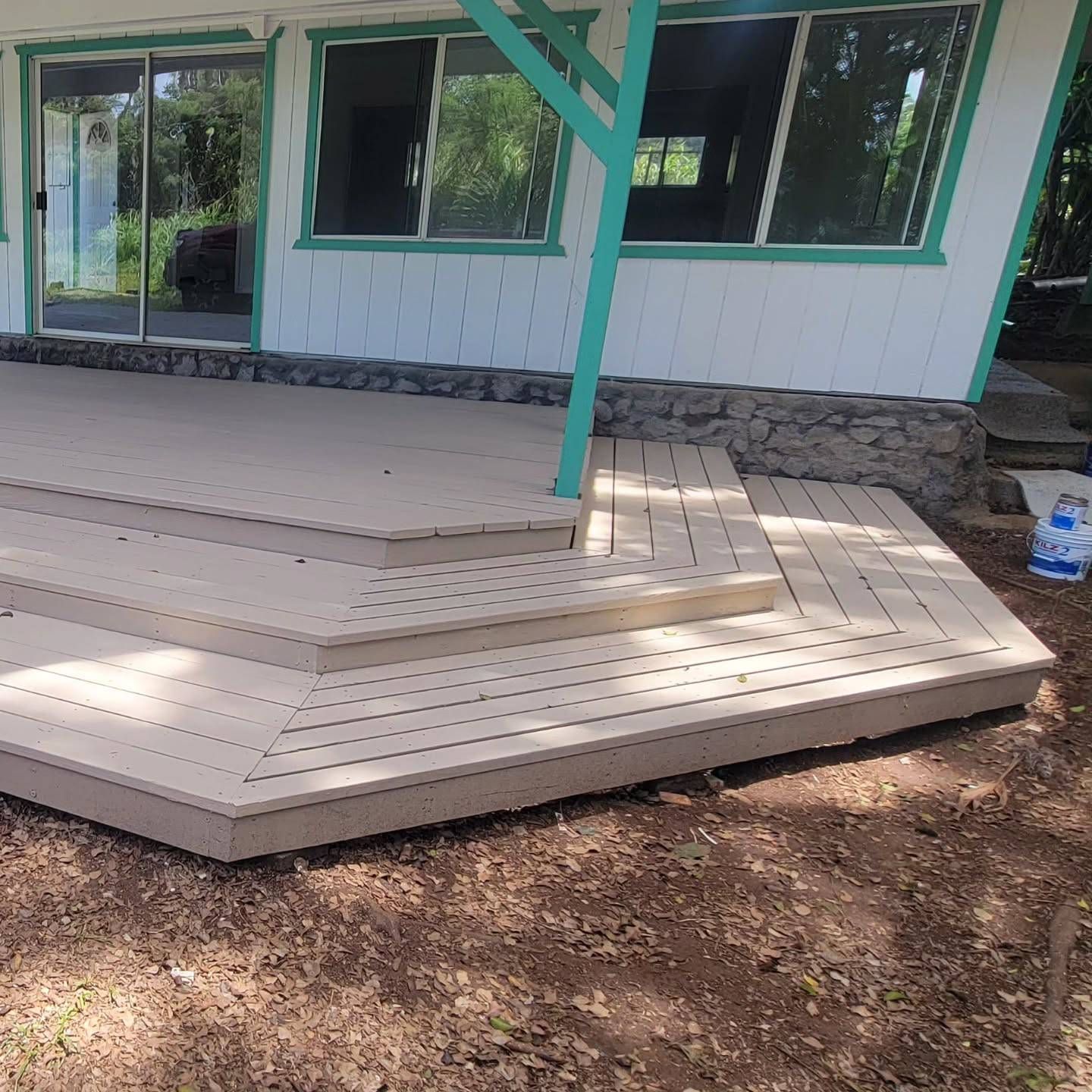 A multi-level light brown deck attached to a white house with teal trim.