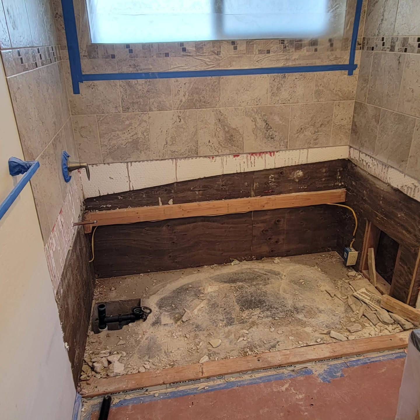 Bathroom remodel in progress; tub area stripped down, exposed wood and mortar. Tile partially installed on walls.