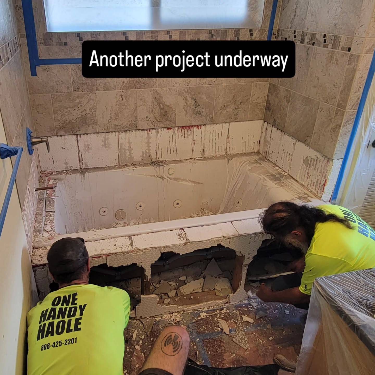 Two people working on a bathroom remodel, removing tile around a tub.