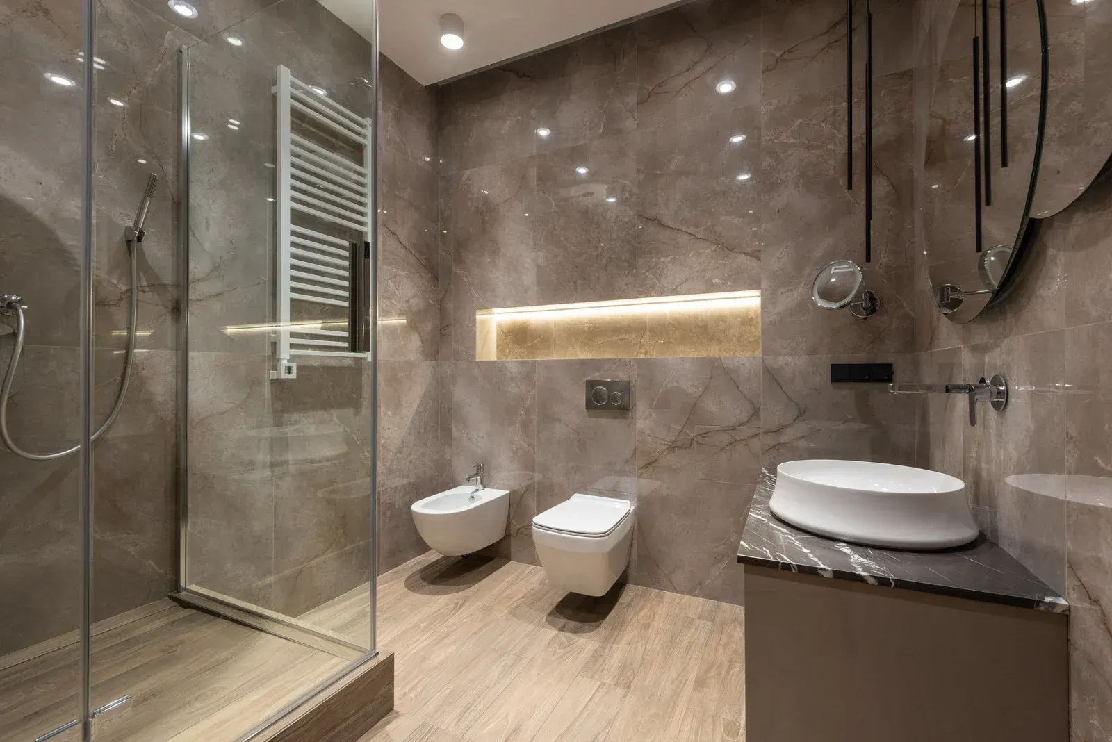 Modern bathroom with marble walls and glass shower. Features toilet, bidet, and vessel sink.