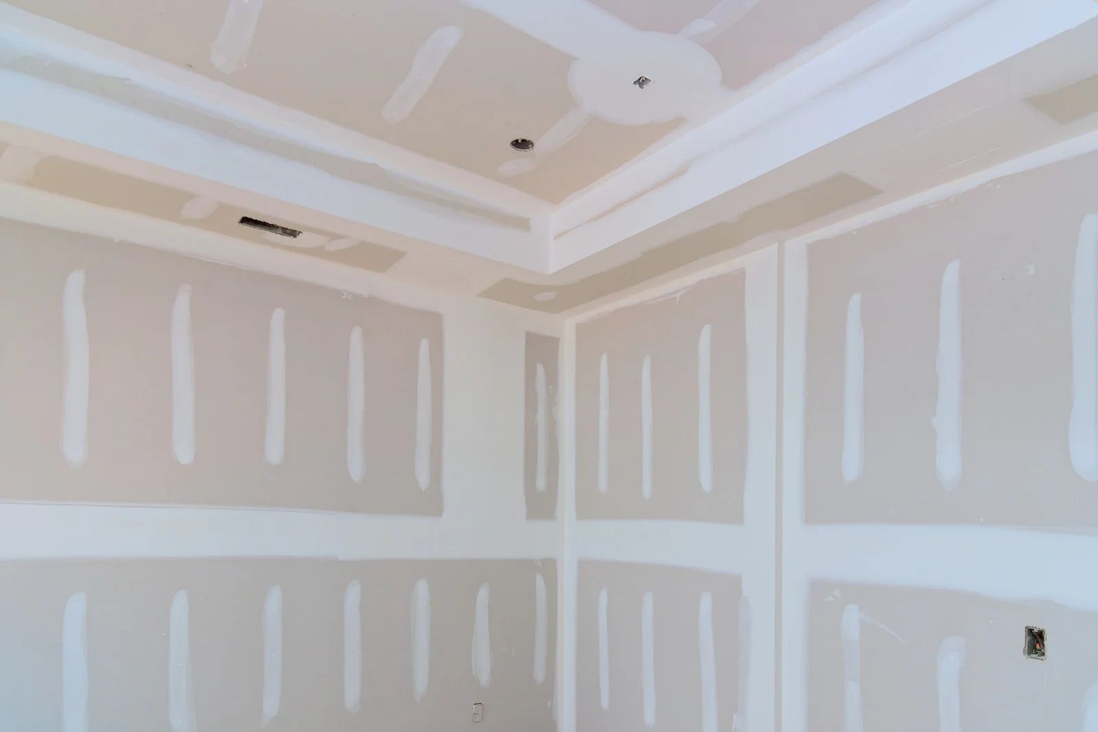 Unfinished room with drywall seams and a white tray ceiling, viewed from a corner.