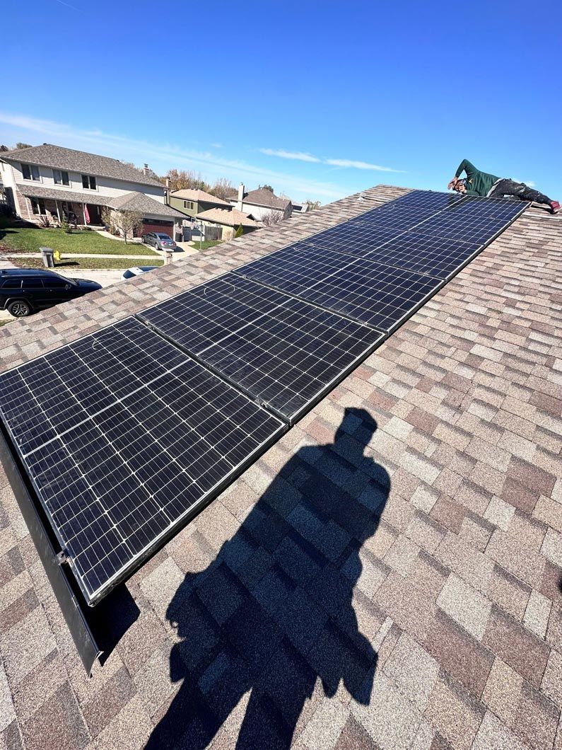 Solar panels installed on a residential roof, blue sky in background, person's shadow on shingles.