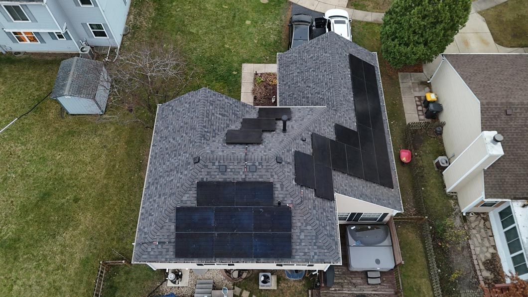 Aerial view of house roof with solar panels installed, surrounded by yard and neighboring houses.