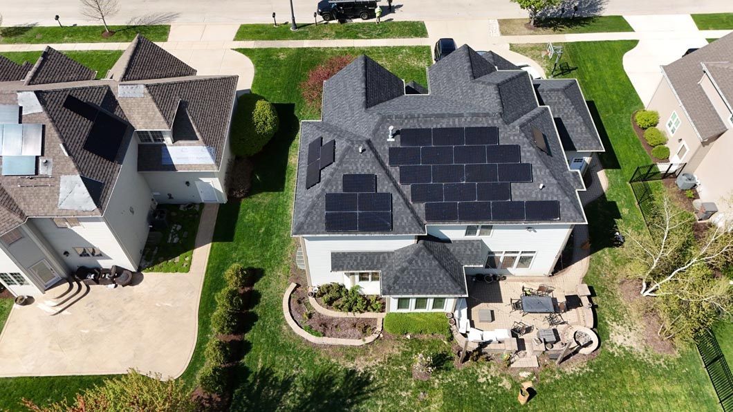 Aerial view of a house with solar panels on the roof, surrounded by green lawn and a stone patio.