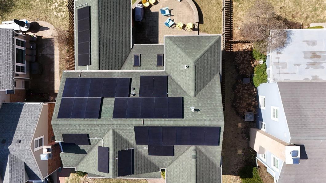Overhead view of a house with solar panels on the roof; green roof, brown siding, and surrounding houses.