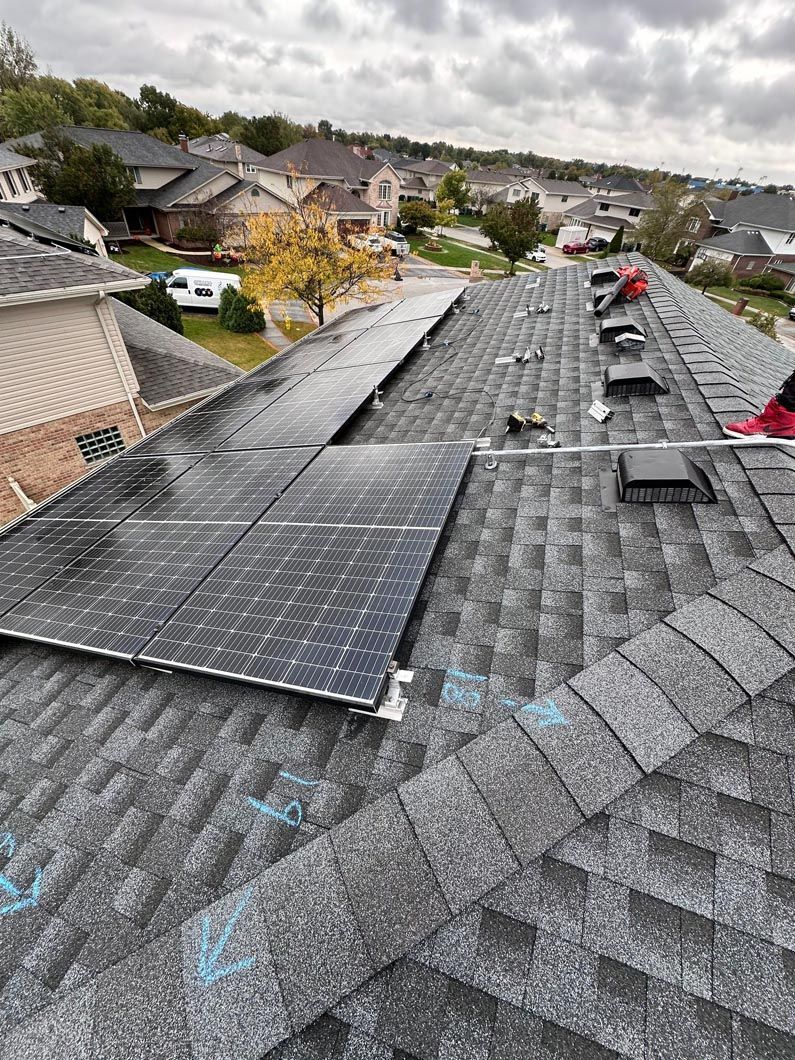 Solar panels being installed on a residential roof in a suburban neighborhood on a cloudy day.