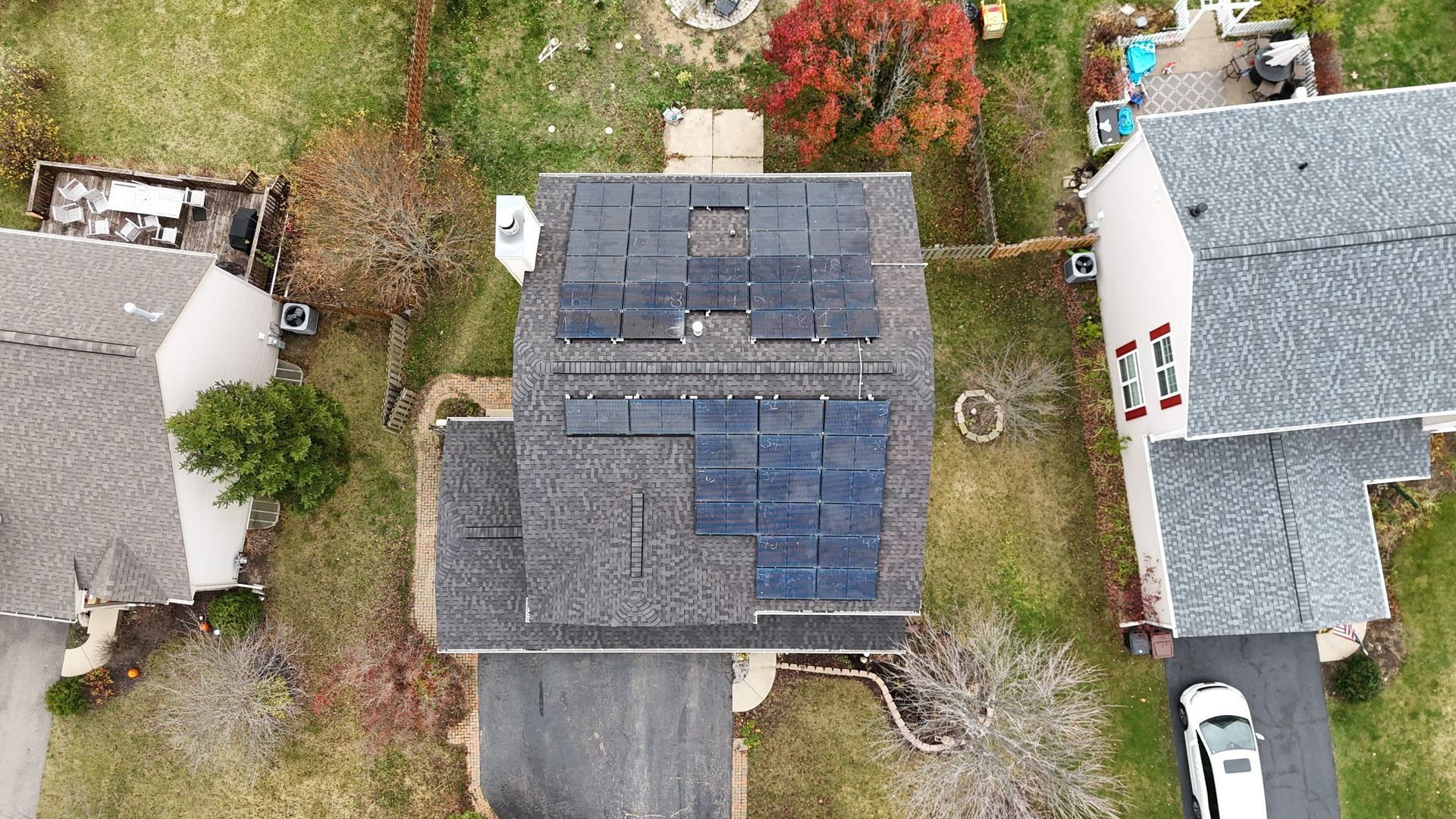 Overhead view of a house with solar panels on the roof; other houses and cars visible.
